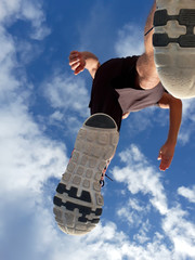 Young man running against the blue sky. Bottom view.