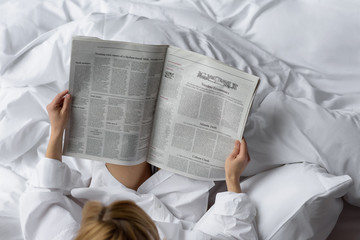 woman reads newspaper in white bedding