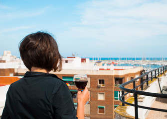 Fototapeta na wymiar Woman look from her balcony on sea in Spain with glass of red wine. Woman in stress.