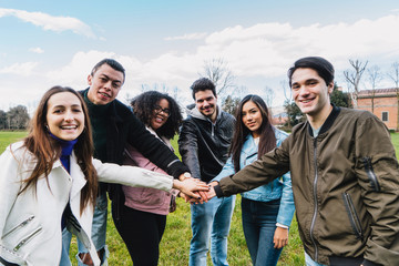Group of young friends at the park join hands in the center of a circle to give unity and strength to everyone - Millennials in a team building moment - People have fun together - 342405283