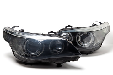 A pair of xenon headlights for a German auto - optical equipment with a lens and corrector inside on a white isolated background. Spare part for replacing a front body part in a car service. - obrazy, fototapety, plakaty