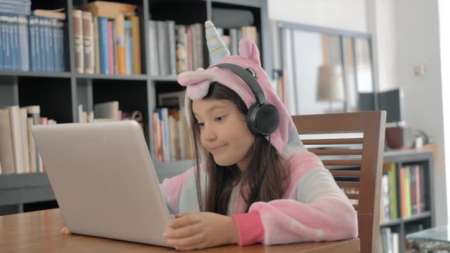 ni&ntilde;a peque&ntilde;a con pijama con capucha usa un port&aacute;til y auriculares para v&iacute;deo grupal con su familia