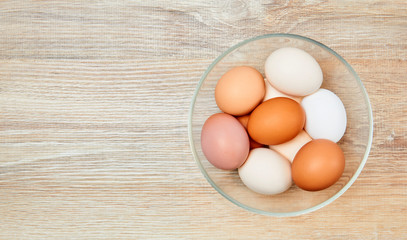 eggs of different colors from white to brown in a glass bowl on a wooden table surface