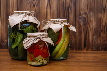 Homemade pickles in glass jars, cucumbers, peppers. Canned vegetables on a wooden background. Preserves. - 342408853