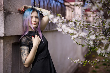 Young blue violet haired girl in black dress in a blooming garden