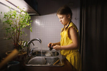 Girl child washes dishes in the kitchen sink
