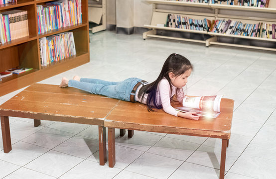 Little girl laying down on wooden table,reading book ,with interested feeling,at school,blurry light around,Leens flare effect