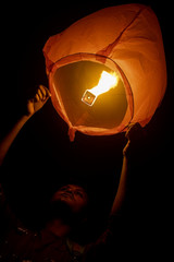 a teenager adult boy holding a sky lantern to launch in black night sky