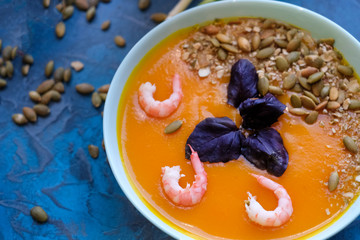close up pumpkin soup with green onions and prawns on a blue background. Top View