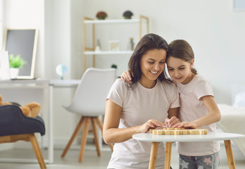 Mother and daughter in pajamas play board games while sitting at a table in the living room.