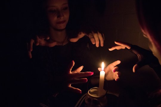 Women Practicing Witchcraft By Burning Candle In Darkroom