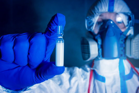 Scientist In Protective Suit And Respirator Holds White Ampoule With Coronavirus Vaccine In His Hand