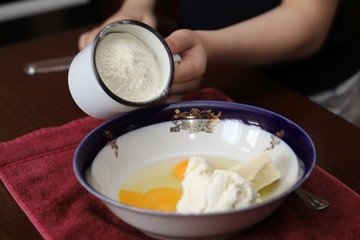 pour flour from a mug into a plate with eggs, sugar, cottage cheese and other ingredients, prepare pizza at home, Easter, cupcake, bake with the child, classes in quarantine