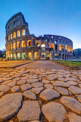 Obraz na płótnie Canvas The illuminated Colosseum in Rome at dawn with big cobblestones in the foreground