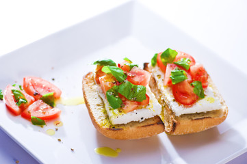 Two sandwiches on a plate, tomato, basil and cheese on bread.