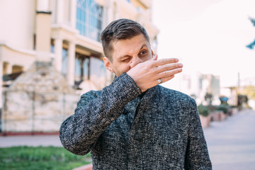 A sick young man with a runny nose wipes his nose with his hand in the street. When protecting against coronavirus or bacteria, you should use napkins or a handkerchief - 342417235