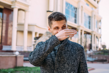 A sick young man with a runny nose wipes his nose with his hand in the street. When protecting against coronavirus or bacteria, you should use napkins or a handkerchief - 342417266