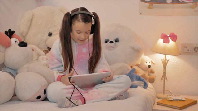 ni&ntilde;a con pijama de unicornio sentada en su habitaci&oacute;n habla feliz con aud&iacute;fonos en conferencia