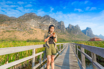 Asian hikers carry heavy backpacking on a small Pavilion outdoor hiking path on a wooden bridge in a swamp with meadows with a blue mountain background. Khao Sam Roi Yot National Park.