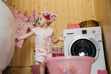 Little girl sitting bathes a doll in a basin on the floor in the bathroom