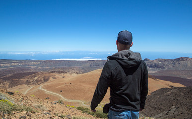 Young man on top of a mountain with amazing panoramic view. Success. Male hiker enjoying the beautiful view from the top. The volcano El Teide in Tenerife, Spain.