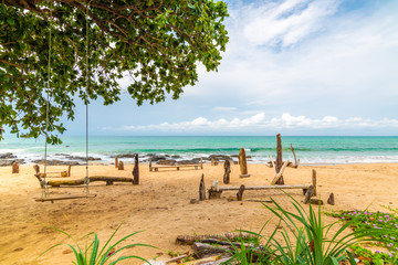 Khlong hin beach at Ko Lanta island, Thailand. View of beach with trees and swing. Place for relaxation near turquoise sea. Tropical plants in foreground. Concept of vacation in tropical paradise.