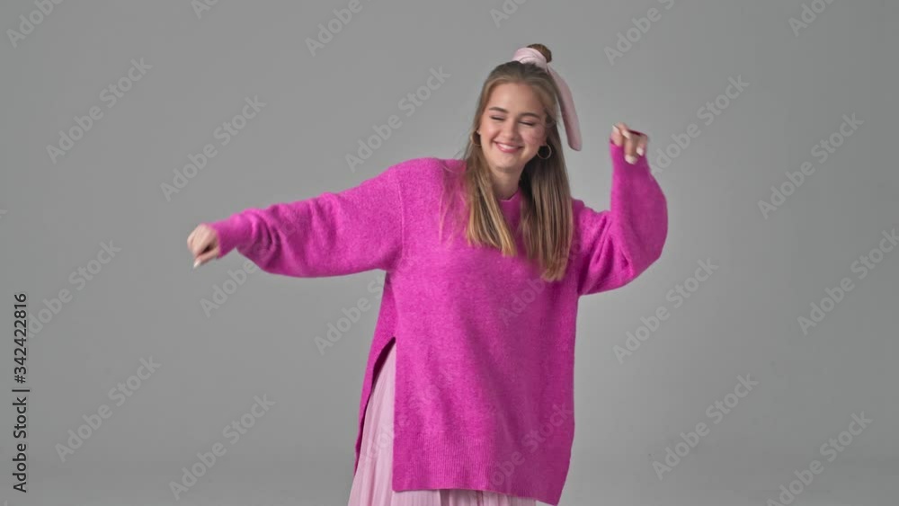 Poster A happy smiling young woman is dancing isolated over grey background in studio