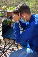 Man wearing a face mask making a video call with the laptop on his balcony, confined at home by the quarantine due to covid-19