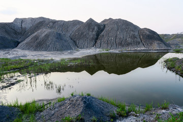 Lake in a coal pit with clear water at sunset. Reflection in the water of a coal mountain, hill,...