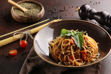 Italian cuisine. Bolognese pasta with tomatoes, basil and spices. Macaroni spaghetti with minced meat in a deep brown plate on a brown background. Menu restaurant. Background image, copy space