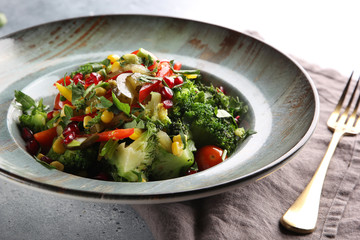 Lean vegetable salad with broccoli, red pepper, corn, cucumber and pomegranate seeds in a deep dish with fork on a light grey background. Background image, copy space