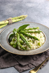Risotto with asparagus in a grey plate. Rice with sauce, basil and asparagus beans on a light grey background with a fork. Lean dish. Background image, copy space