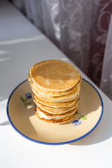 A plate with a homemade pancake on the windowsill. Plate with a breakfast. Sunny morning. Healthy food.