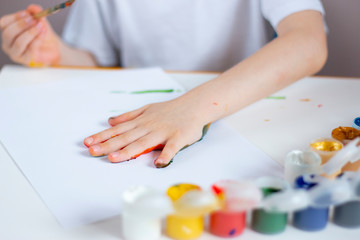 Obraz na płótnie Canvas The child makes an imprint of his palm on a white sheet of paper. Children's creativity.