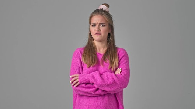 A irritated young woman is gesturing with raised hands while arguing isolated over a grey background in studio