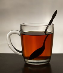 Transparent Cup with tea and a teaspoon on a grey background.