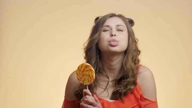 funny girl with caramel candy teasing showing tongue on colored studio background, young happy woman with sweet lollipop