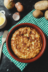 Spanish omelette in a wooden plate with all the ingredients to make it. Top view of Spanish omelette on a table with a checkered tablecloth
