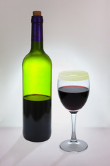 A glass of dark red wine and an incomplete bottle of green glass wine, lit from behind with bright light. Defocused Background. Selective focus