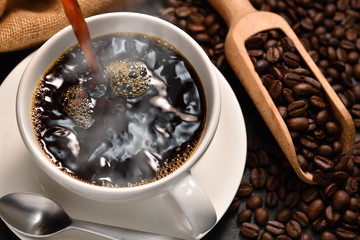 Fototapety  Nalewanie kawy z dymem na filiżankę i ziarna kawy na jutowy worek na czarnym tle