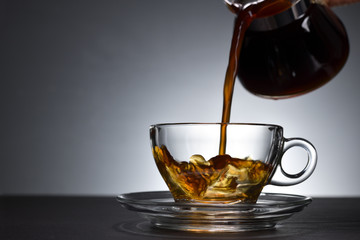 Pouring coffee on a transparent cup on black background