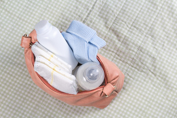 Small pink diaper bag on changing pad. First care baby accessories with bottle. Soft green background. Top view. Newborn and maternity concept.