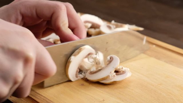Hands of a woman cutting mushrooms on a wooden Board. Close up