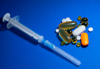 capsules, tablets and a syringe with a needle on a plain blue background. The concept COVID19
