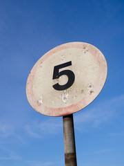 Badly sun-bleached 5mph road speed sign, against blue sky, in England.
