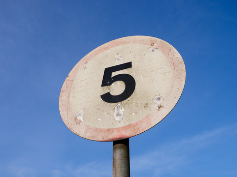 Badly sun-faded 5mph road speed sign, against blue sky, in the UK.