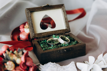 Wedding rings lie in a wooden box on a flower.