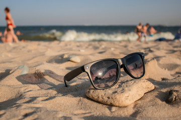 Fototapeta na wymiar Sunglasses on the rock on the sand on the sea beach with the sunlight with the sea on the background