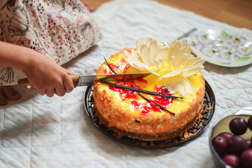 A girl cuts her delicious holiday cake with a knife. Beautiful birthday cake at home.