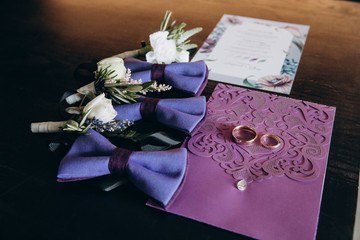 Details of the wedding day of the newlyweds. The rings of the bride and groom lie together with the inviting and boutonniere on the table.